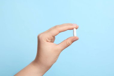 Açık mavi arka planda hap tutan kadın, yakın plan.