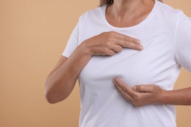 Açık kahverengi arka planda göğüs muayenesi yapan kadın, yakın plan. Metin için boşluk