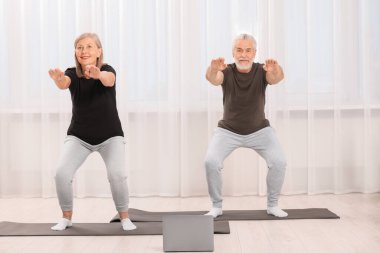 Üst düzey çift evde dizüstü bilgisayarla yoga yapıyor.