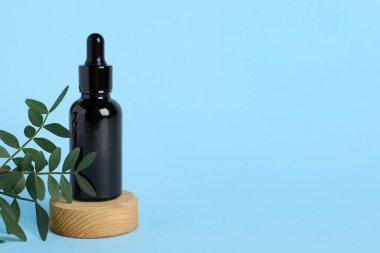 Podyumda kozmetik yağlı şişe ve açık mavi arka planda yeşil dal, metin için boşluk