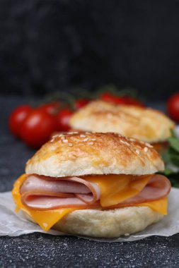 Koyu gri desenli masada jambonlu ve peynirli lezzetli simit, yakın plan.