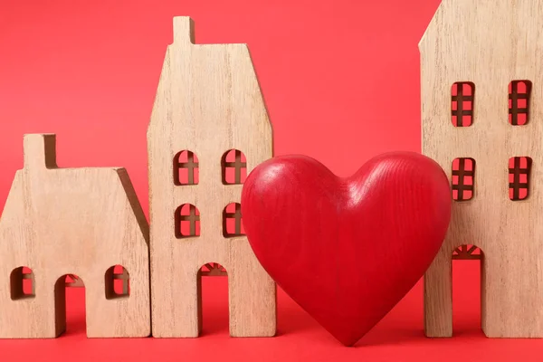 Long-distance relationship concept. Wooden house models and decorative heart on red background, closeup