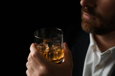 Siyah arka planda buzlu viski bardağı tutan adam, yakın plan.