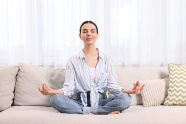 Evdeki kanepede meditasyon yapan bir kadın. Ahenk ve zen