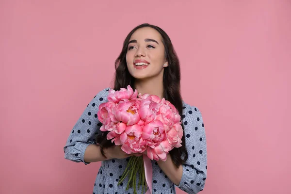 ピンクの背景に牡丹の花束を持つ美しい若い女性 — ストック写真