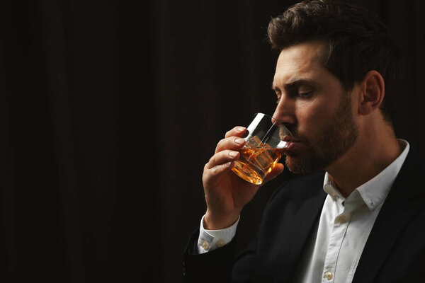 Man in suit drinking whiskey on black background. Space for text