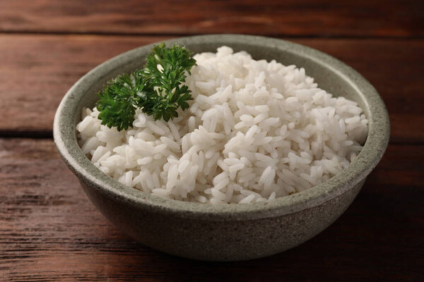 Delicious rice with parsley in bowl on wooden table, closeup