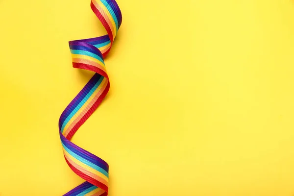 Rainbow ribbon on yellow background, top view with space for text. LGBT pride