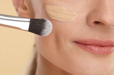 Bej arka planda fırçayla fondöten kadın, yakın plan