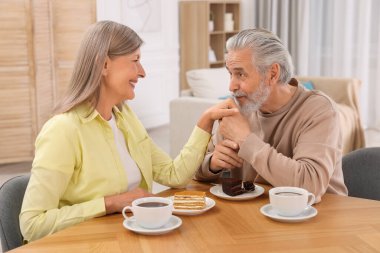 Sevecen yaşlı çift odasındaki ahşap masada kahvaltı yapıyor.