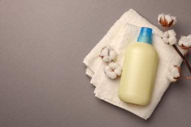 Bir şişe yumuşatıcı, havlu ve gri arka planda güzel pamuk çiçekleri, üst manzara. Metin için boşluk
