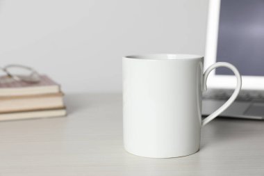 Beyaz ahşap masada içki ve dizüstü bilgisayarlı bir seramik bardak, mesaj için yer var.