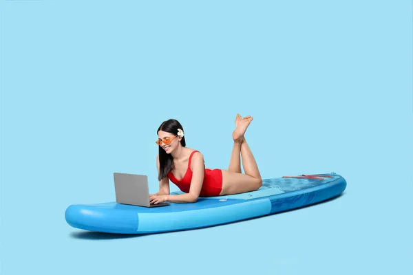 Happy woman with laptop on SUP board against light blue background