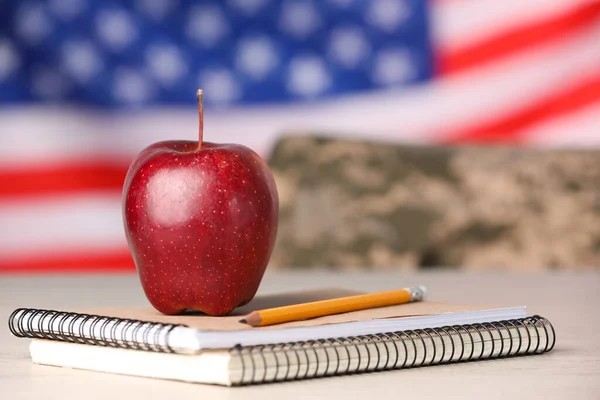 Notebooks, apple and pencil on light table against flag of USA. Military education