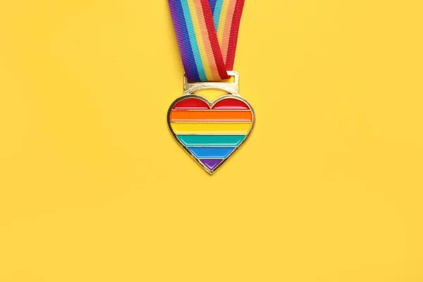 Rainbow ribbon with heart pendant on yellow background, top view and space for text. LGBT pride