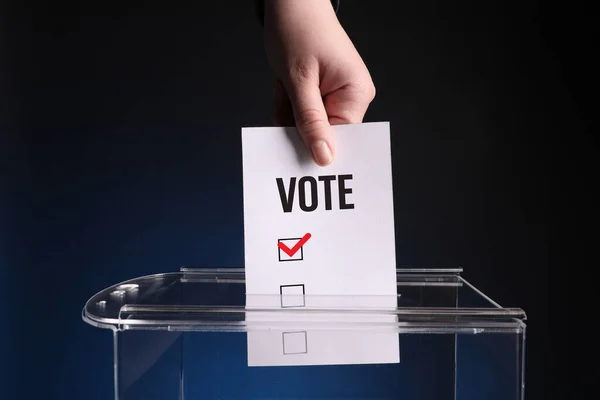 ダークブルーの背景に投票ボックスに紙を貼る女性 — ストック写真