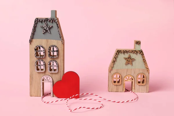 Decorative heart and cord between two house models on pink background symbolizing connection in long-distance relationship