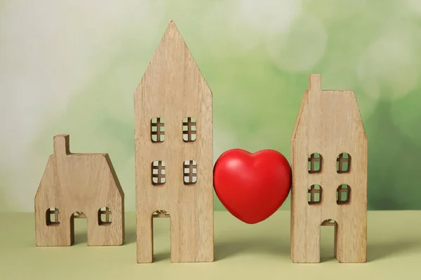 Long-distance relationship concept. Decorative heart between two wooden house models on light green background