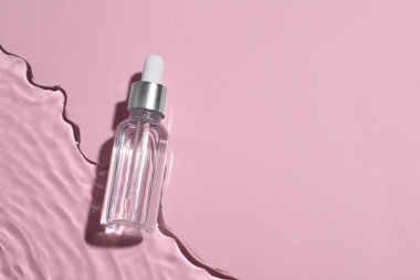 Pembe arka planda suda bir şişe kozmetik yağı, üst manzara. Metin için boşluk