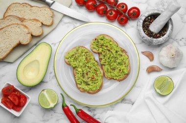 Guacamole soslu lezzetli sandviçler ve beyaz mermer masada malzemeler.