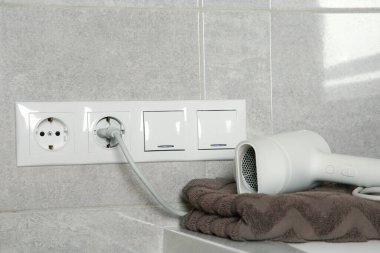 Hairdryer plugged into power socket on light grey wall clipart