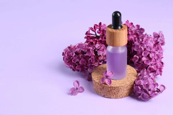 Bottle with essential oil and lilac flowers on violet background, space for text