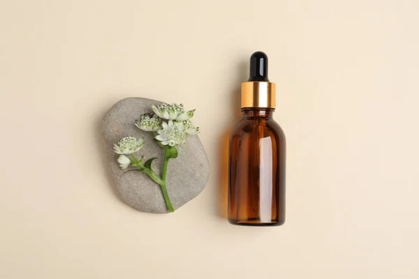 Bottle with cosmetic oil, stone and flower on beige background, flat lay