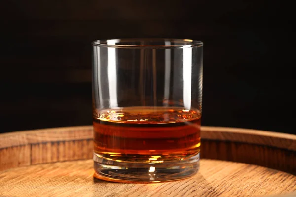 stock image Glass of tasty whiskey on wooden barrel, closeup