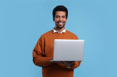 Happy man with laptop on light blue background