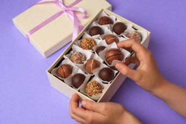 Açık mor arka planda bir kutu lezzetli çikolata şekeri olan çocuk, yakın plan.