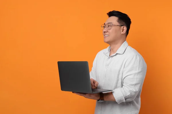 Happy man with laptop on orange background, space for text