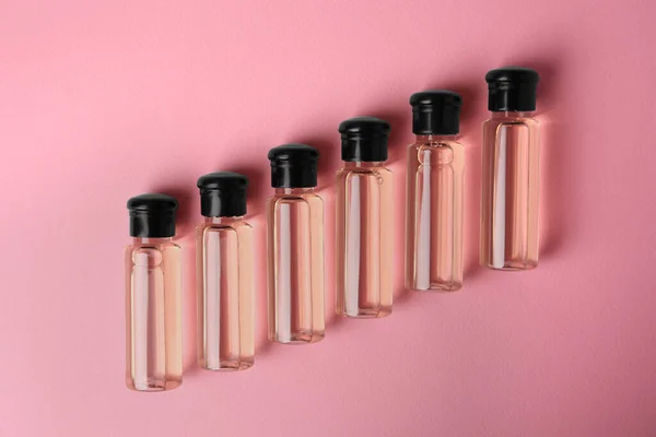 Bottles of cosmetic products on pink background, flat lay