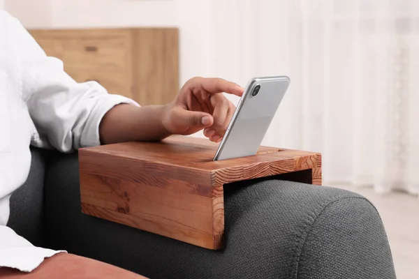 Man using smartphone on sofa armrest wooden table at home, closeup