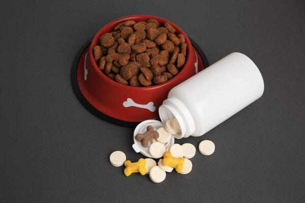 Bottle with vitamins and dry pet food in bowl on grey background, above view