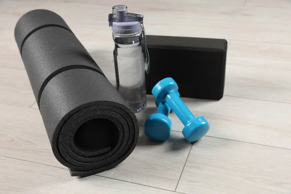 Exercise mat, yoga block, dumbbells and bottle of water on light wooden floor
