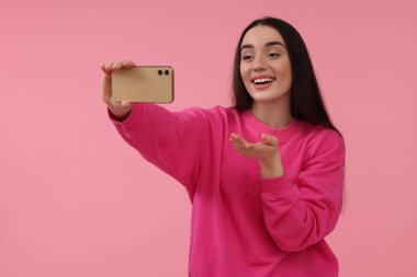 Gülümseyen genç bir kadın pembe arka planda akıllı telefonuyla selfie çekiyor, mesaj için yer var.