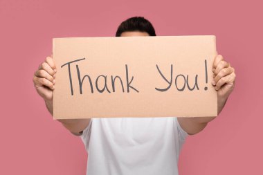 Man holding cardboard sheet with phrase Thank You on pink background, selective focus clipart