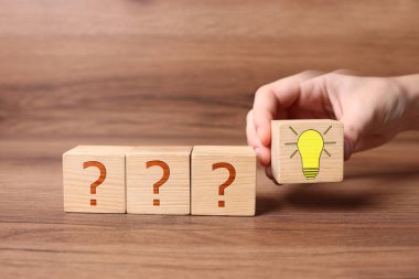 Fikir konsepti. Bir kadın, ahşap masa üzerinde soru işaretleri olanlara ampul resimleriyle küp yerleştiriyor, yakın plan.
