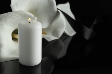 Karanlıkta siyah ayna yüzeyinde yanan mum ve beyaz zambak çiçekleri, metin için yeri olan yakın plan. Cenaze sembolü