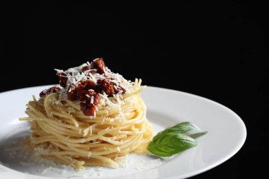 Siyah arka planda, güneşte kurutulmuş domatesli ve parmesan peynirli lezzetli spagetti, yakın plan. Makarna yemeğinin enfes sunumu