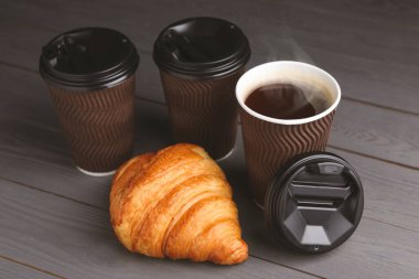 Paket kahve. Lezzetli sıcak içecekle kağıt bardaklar ve gri ahşap masada kruvasan.