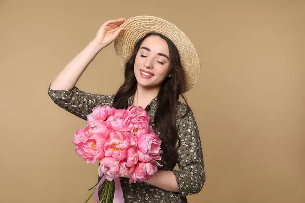 美しいです若いです女性でわら帽子でピンク牡丹の花束とともにライトブラウンの背景 — ストック写真