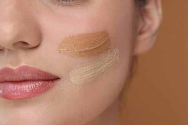 Woman with swatches of foundation on face against brown background, closeup