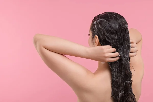 Woman washing hair on pink background, back view