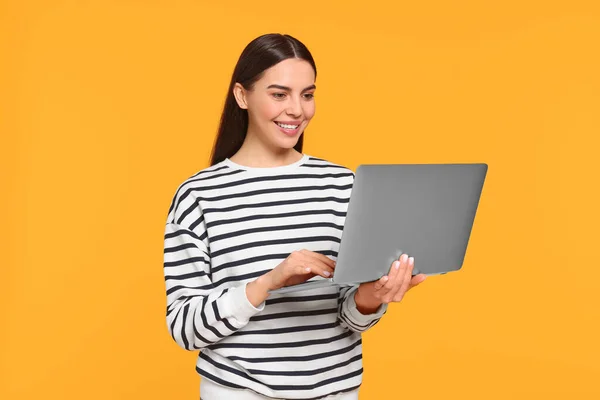 Happy woman using laptop on orange background