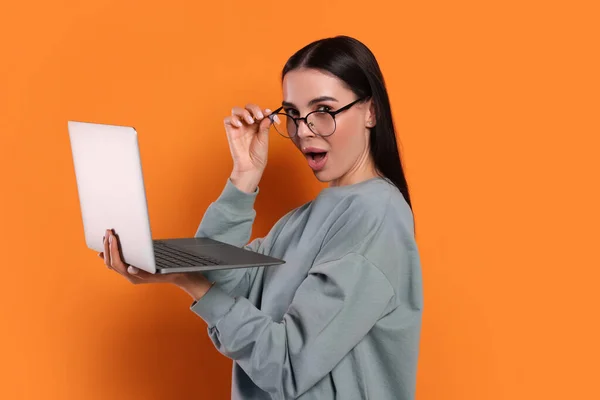 Surprised woman with laptop on orange background