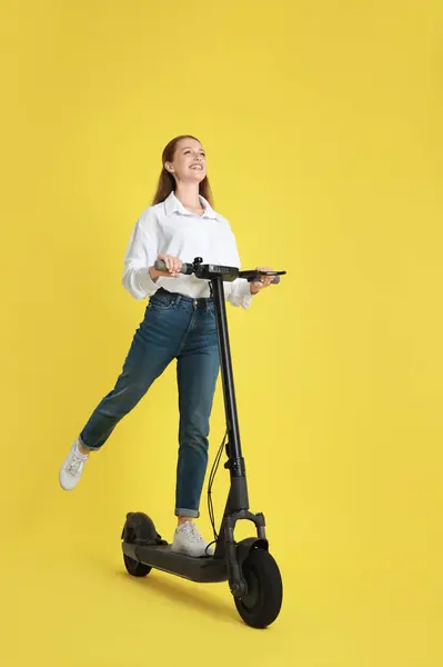 黄色の背景にモダンな電気キックスクーターに乗っている幸せな女性 — ストック写真