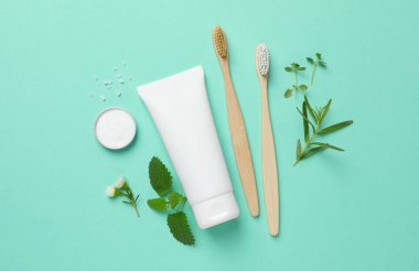 Bambu diş fırçaları ve turkuaz arka planda bitkilerle bezenmiş düz bir bileşim
