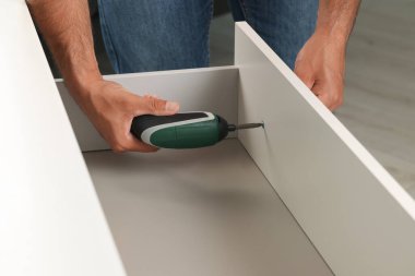 Elektrikli tornavidalı adam çekmece monte ediyor, yakın plan.
