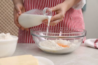 Lezzetli baklava hazırlıyorum. Açık gri masada un ve yumurtalarla kaseye süt döken kadın, yakın plan.